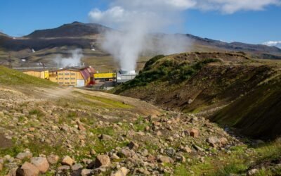 Geothermal plant buildings with steam rising on a rocky hillside.
